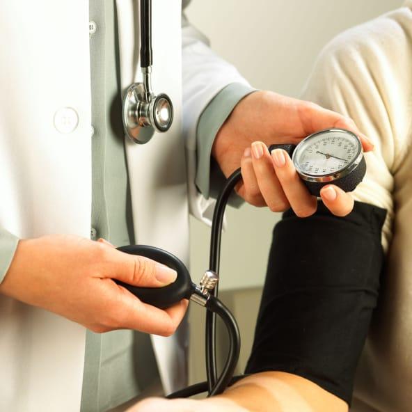 A clinician in a white coat checking a patient's blood pressure with a cuff and gauge