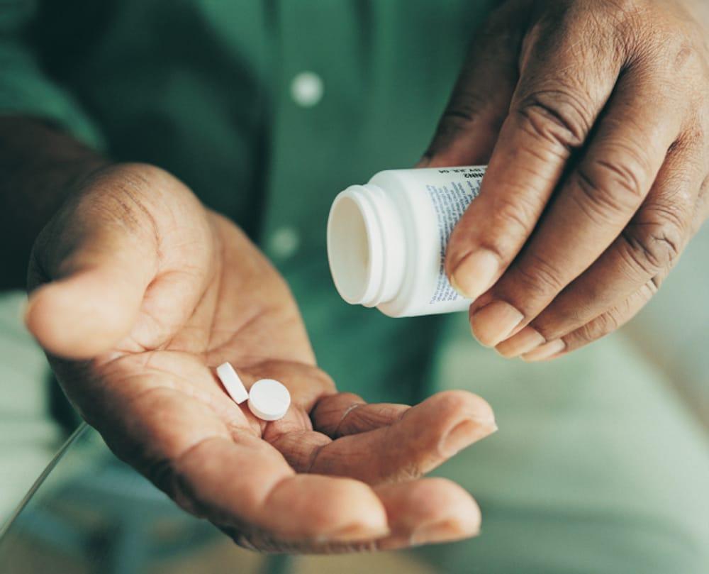 Close-up of a person's hands tipping two white pills from a prescription bottle into their palm