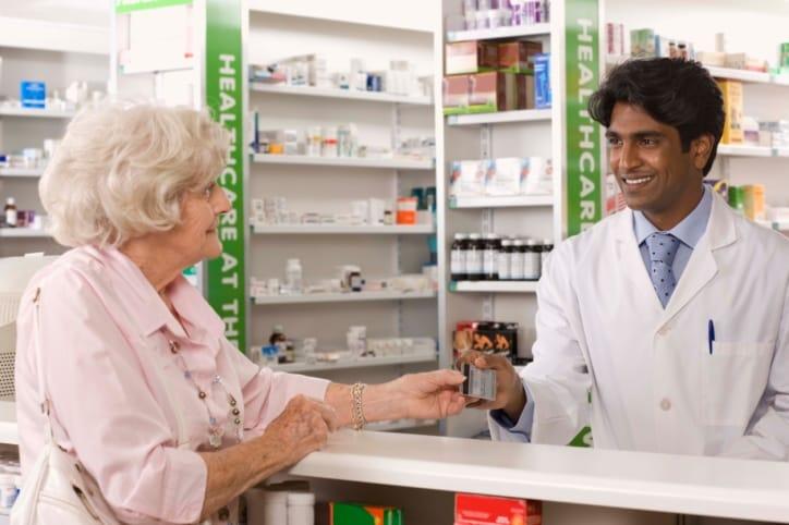 An older woman at a pharmacy counter talking with a smiling pharmacist