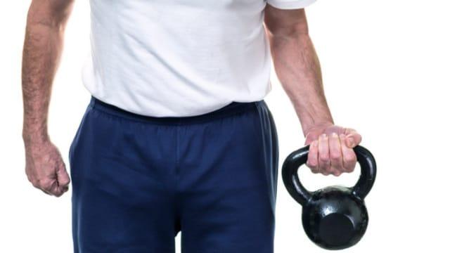 A man in a white T-shirt carrying a kettlebell in one hand at his side