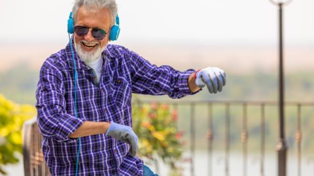 A smiling older man with headphones and sunglasses dancing outdoors