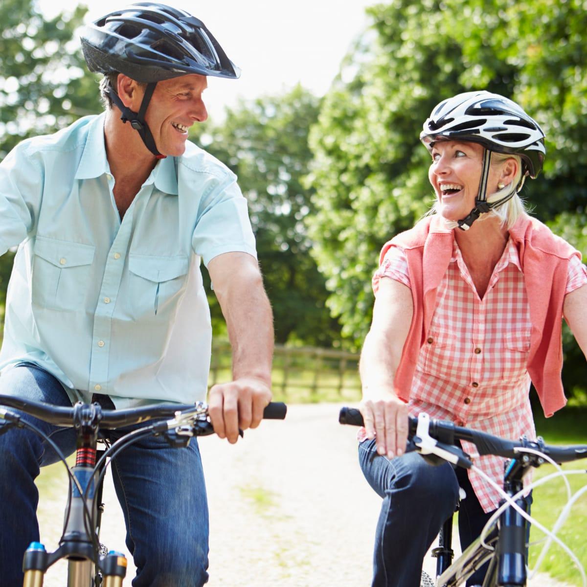 A smiling older couple in helmets riding bicycles along a country path