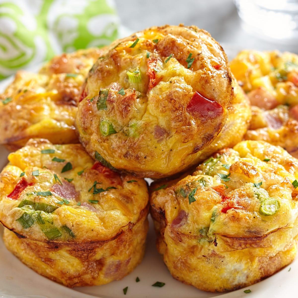A stack of golden baked egg muffins with red peppers and green onions