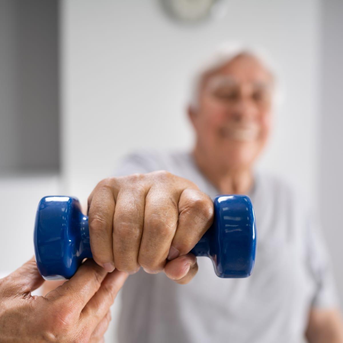 A trainer helping a smiling older man lift a light dumbbell