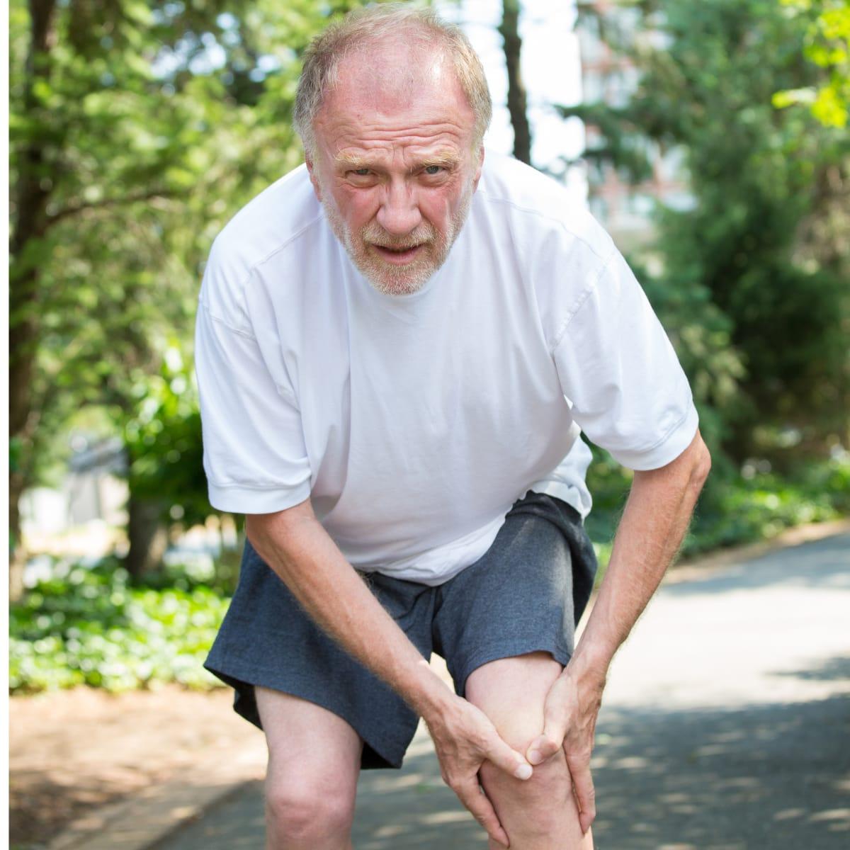 An older man on a walking path grimacing and holding his sore knee