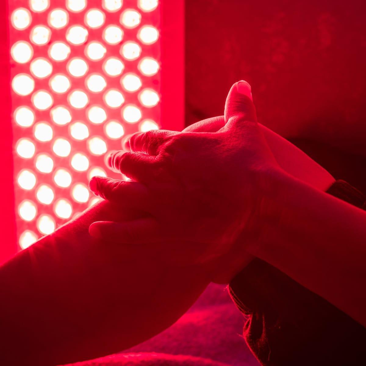 Hands clasped in front of a glowing red light therapy panel