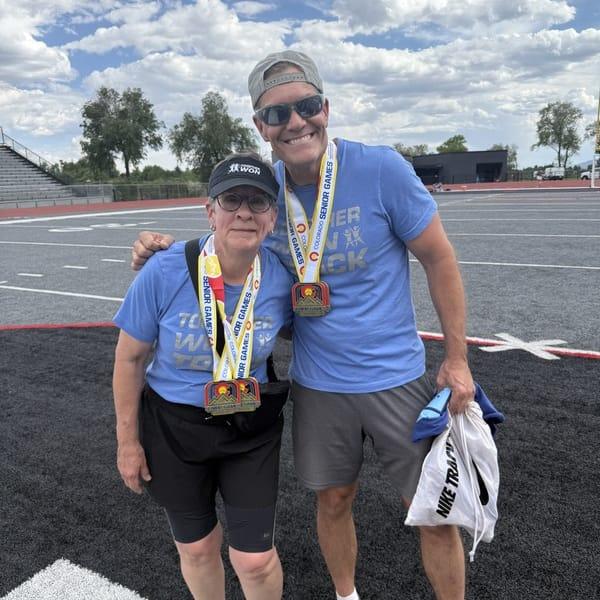 Karol and Aaron smiling on the field, both wearing Senior Games medals