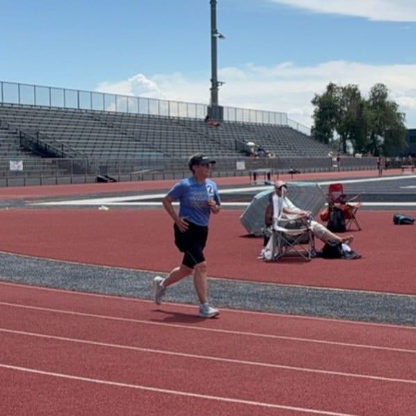 Karol running around the curve of a red track toward the finish, with spectators seated on the infield
