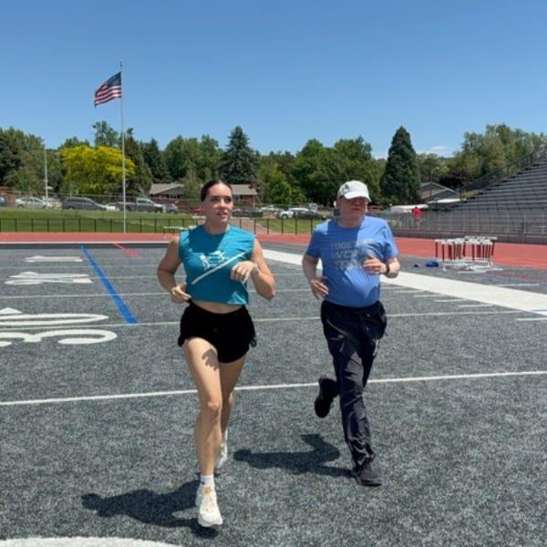 TogetherWON trainer Heidi jogging across a sunny stadium field alongside Richard