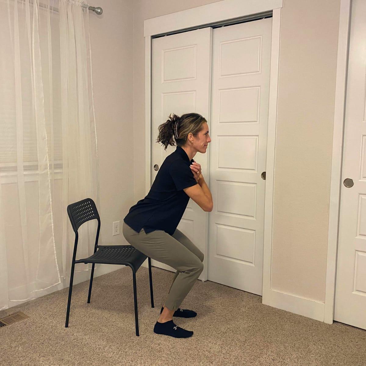 A trainer lowering into a squat in front of a chair with her hands at her chest