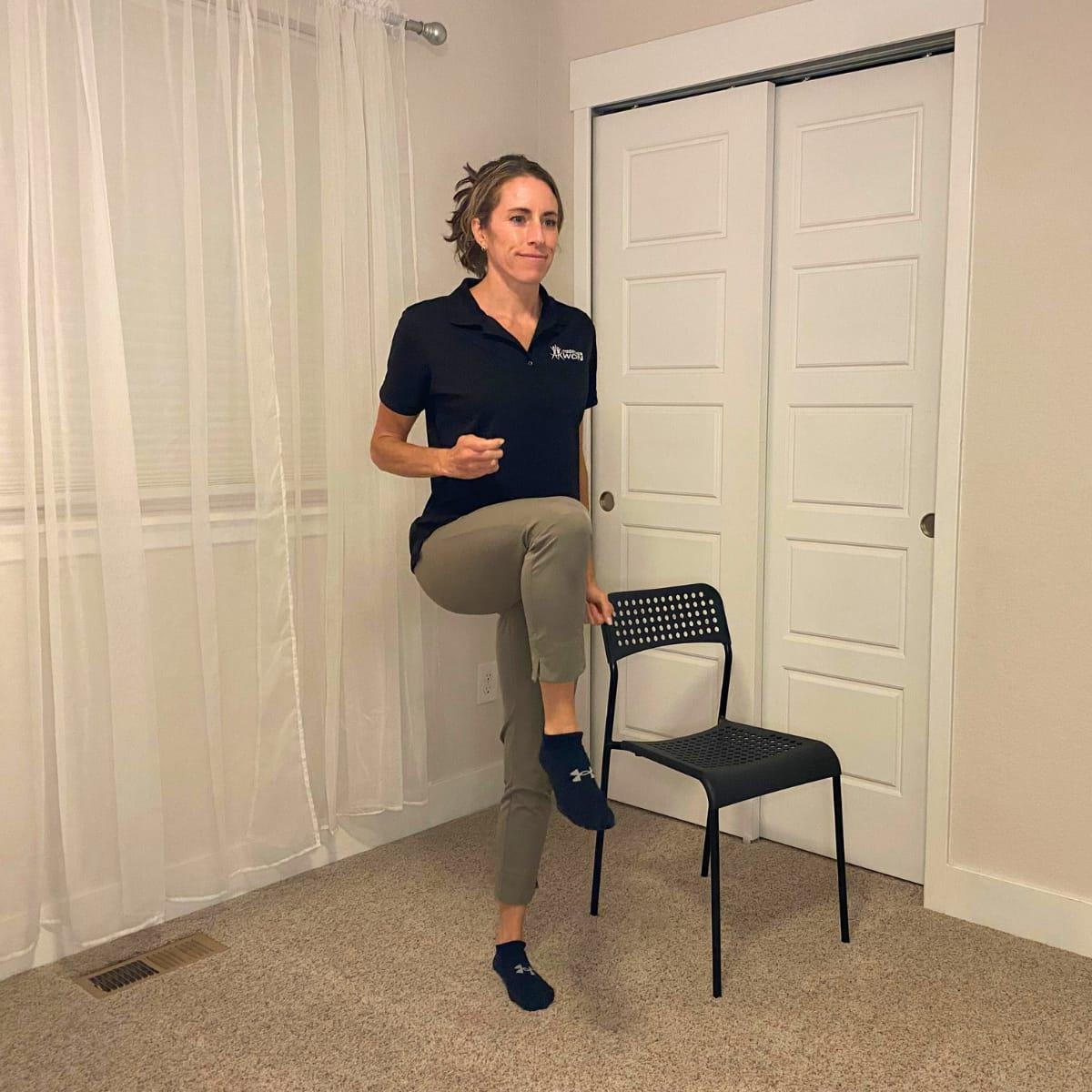 A trainer marching in place, lifting one knee high beside a chair