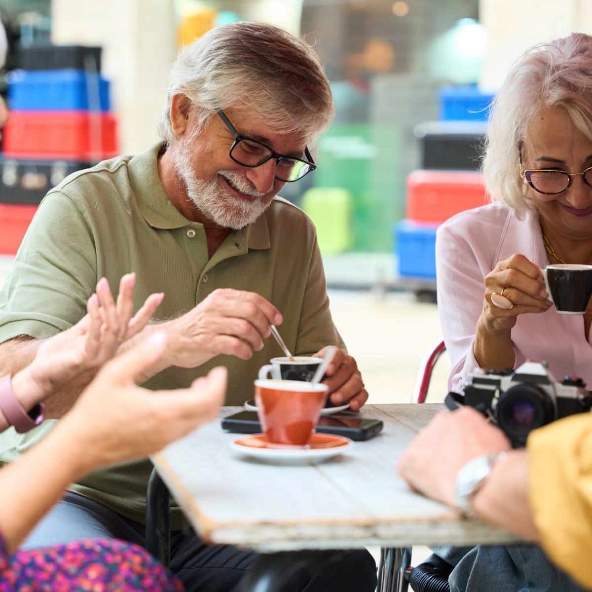 A group of older friends smiling and chatting over espresso at an outdoor café table