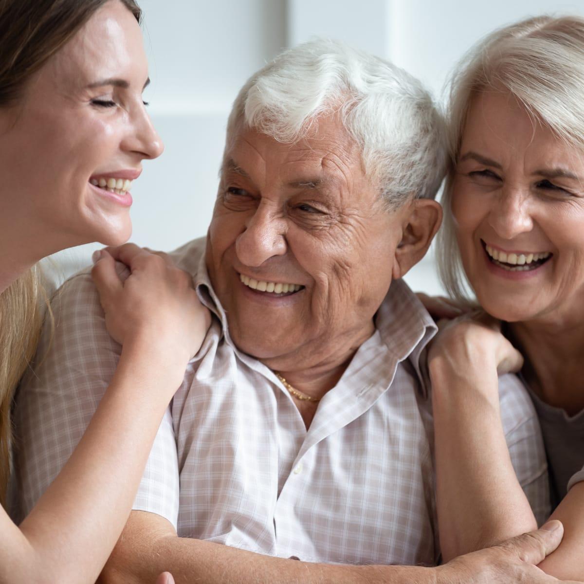 A smiling older man hugged by two laughing women, a younger woman and an older woman