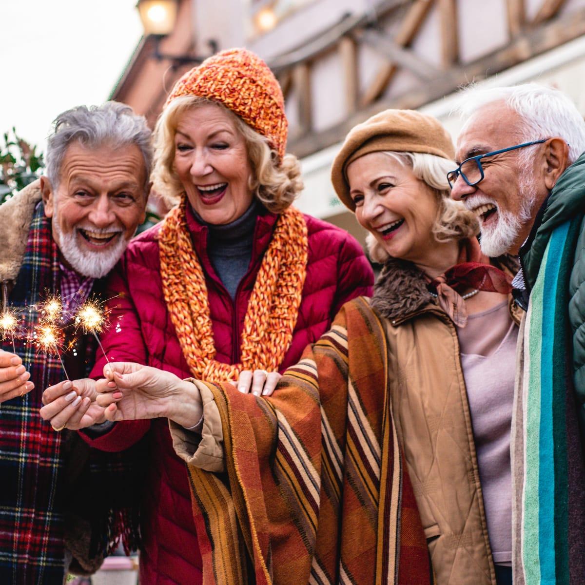 Four laughing older friends in winter coats and scarves holding sparklers outdoors