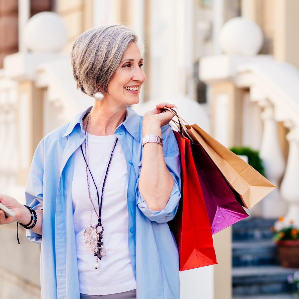 A smiling woman with short gray hair carrying colorful shopping bags over her shoulder