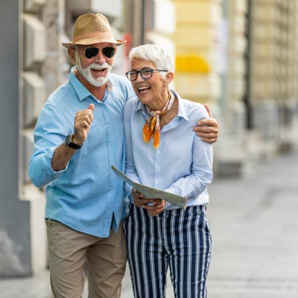 An older couple laughing together on a city sidewalk, holding a map