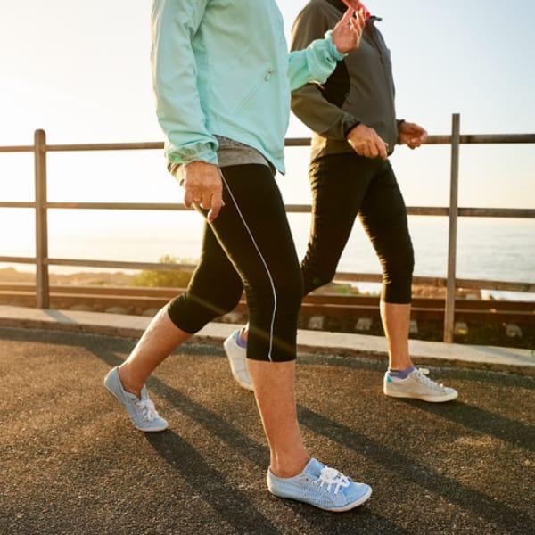 Two people in athletic wear walking side by side along a seaside path at sunrise