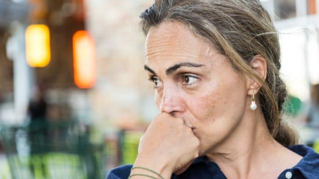 A worried woman gazing into the distance with her fist pressed to her lips