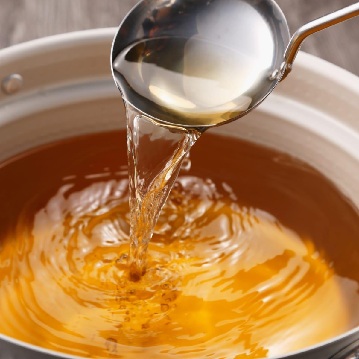 A ladle pouring clear golden broth back into a large pot
