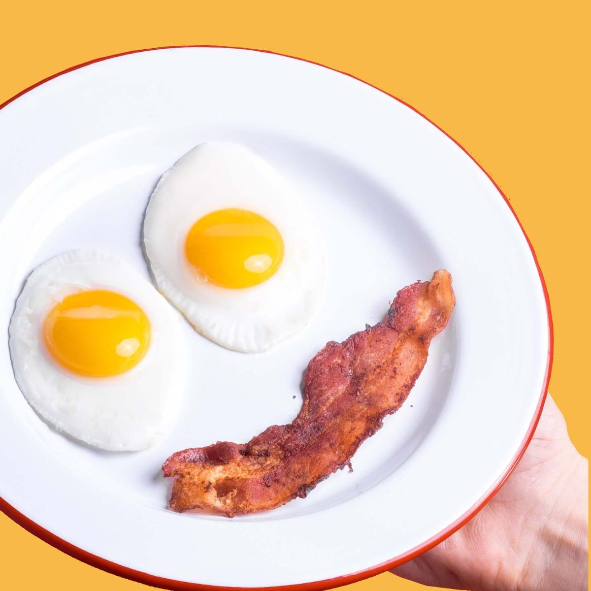 Two sunny-side-up eggs and a strip of bacon arranged like a smiley face on a white plate