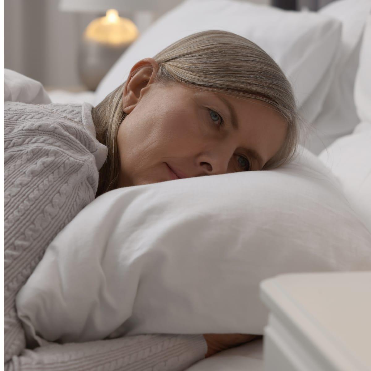 A woman lying awake in bed with her head on a white pillow