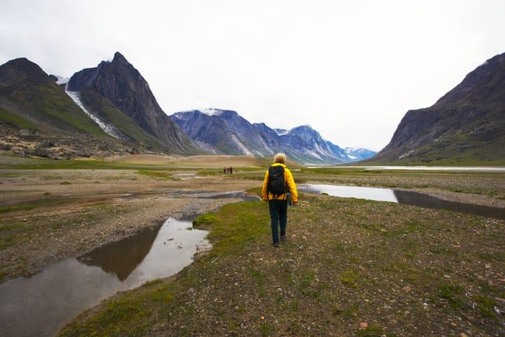 A hiker in a yellow jacket walking through a wide mountain valley