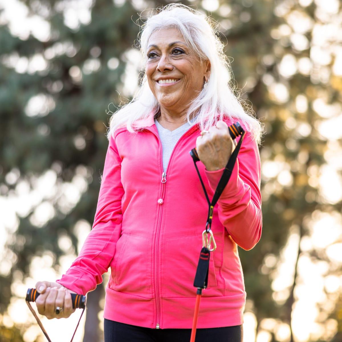 A smiling older woman doing bicep curls with a resistance band outdoors