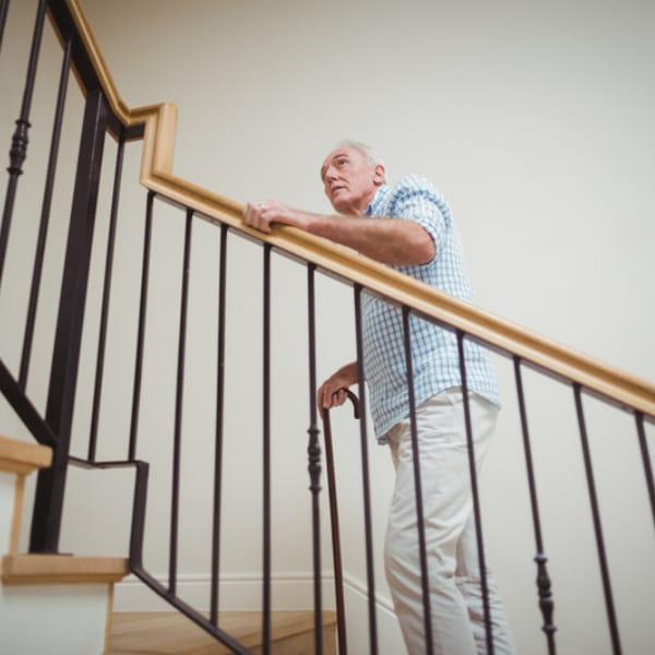 An older man with a cane holding the handrail as he climbs a staircase