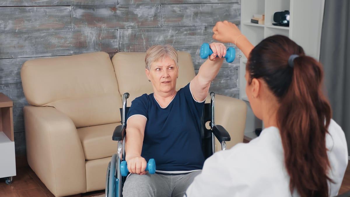 Trainer guiding a senior woman through dumbbell exercises in her living room