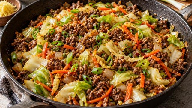 A cast-iron skillet of ground beef with shredded cabbage, carrots and sliced green onions