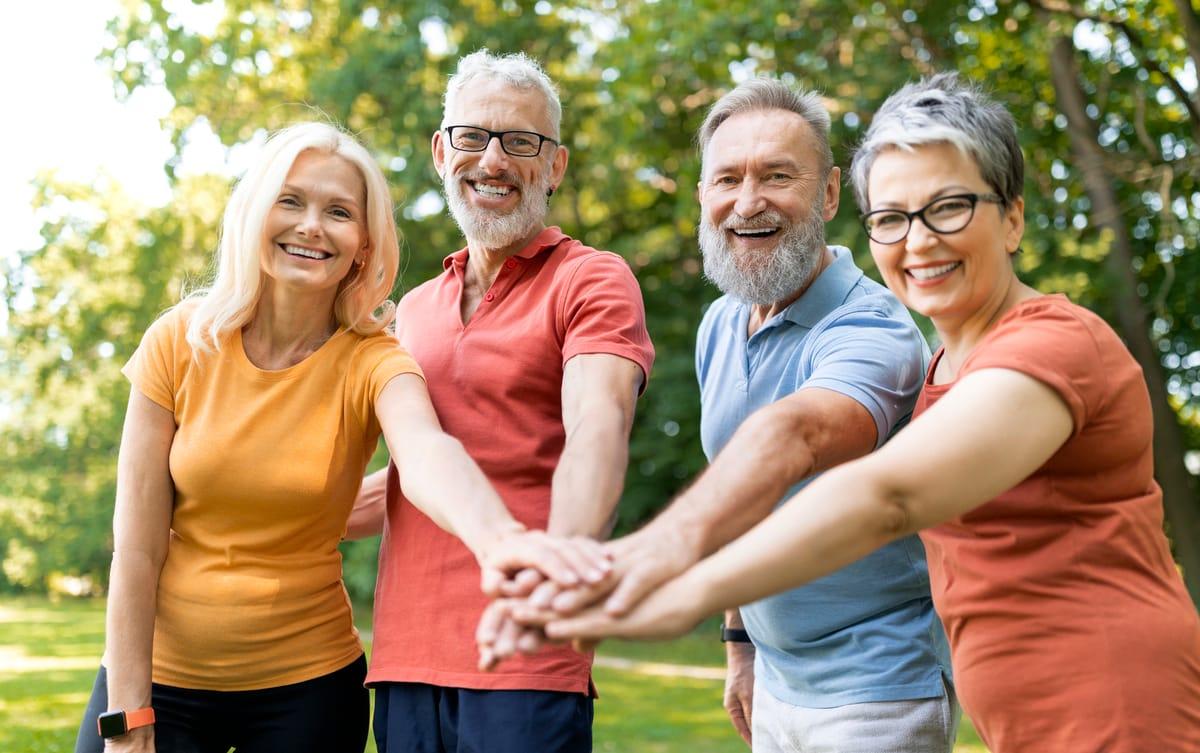 Four smiling older adults stacking their hands together outdoors